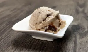 Ein Löffel cremiges Tiramisu Eis mit dunklen Schokoladenstreifen in einer weißen Schale auf Holzhintergrund.