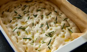 Luftiger focaccia teig mit Rosmarin und Olivenöl in einer Backform, bereit zum Backen.