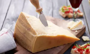 Ein großes Stück Parmesan mit einem Messer, daneben Bruschetta und ein Glas Rotwein.