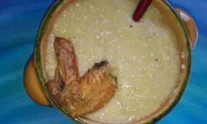 Herzhafte polenta taragna mit einem knusprigen Hähnchenflügel in einer rustikalen Schüssel.