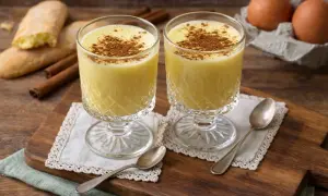 Zwei Gläser cremiges Zabaione ohne Alkohol, bestreut mit Zimt. Dazu Savoiardi-Kekse und Zimtstangen.