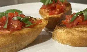 Drei Bruschetta-Scheiben mit Tomaten und Basilikum auf einem Teller.