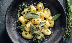 Salbei Gnocchi mit frischen Kräutern und Parmesan bestreut, serviert auf einem dunklen Teller.
