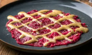 Rotes Carpaccio auf dunklem Teller mit gelber Sauce und Pfeffer bestreut.