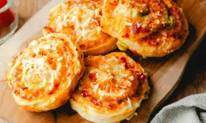 Leckere Pizzaschnecken aus Pizzateig, überbacken mit Käse und Tomaten, liegen auf einem Holzbrett.