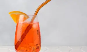 Ein Aperol Spritz mit Orangenscheibe und braunem Strohhalm auf Eis.