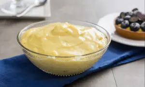 Cremige, vanilleschotenhaltige Crema Pasticcera in einer Glasschüssel, daneben ein Blaubeer-Törtchen.
