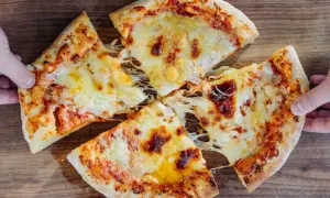 New York Style Pizza mit geschmolzenem Käse, von Händen gehalten, auf Holzuntergrund.