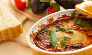 Gebackene Auberginen mit Tomatensoße und Basilikum in einer Auflaufform, daneben Parmesan und frische Auberginen.
