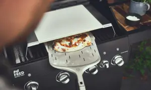 Frisch gebackene Pizza auf dem Gasgrill, bereit zum Servieren. Der Pizzastein liegt auf dem Grill, während die Pizza auf einem Pizzaschieber ruht.
