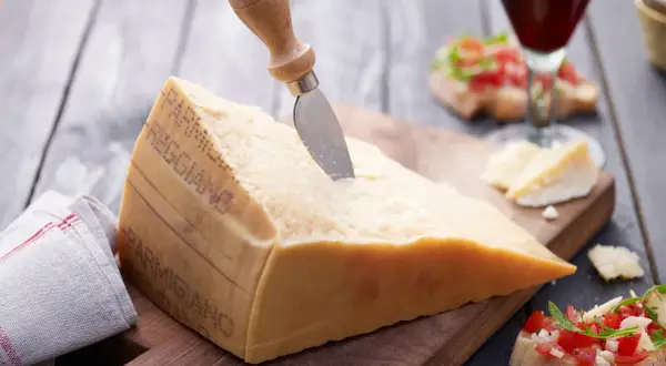Ein großes Stück Parmesan mit einem Messer, daneben Bruschetta und ein Glas Rotwein.