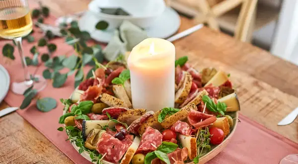Antipasti-Platte mit Kerze, Wurst, Käse, Brot, Oliven und Tomaten.