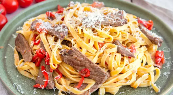 Pasta mit Rinderfiletstreifen, garniert mit geriebenem Parmesan und roten Paprikastücken. Ein köstliches Gericht, das zum Genießen einlädt.