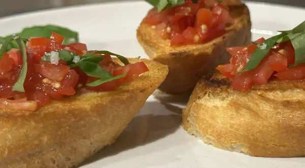Drei Bruschetta-Scheiben mit Tomaten und Basilikum auf einem Teller.