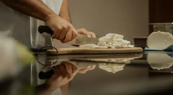 Hände schneiden frischen Käse, eine köstliche fior di latte Alternative, auf einem Holzbrett.
