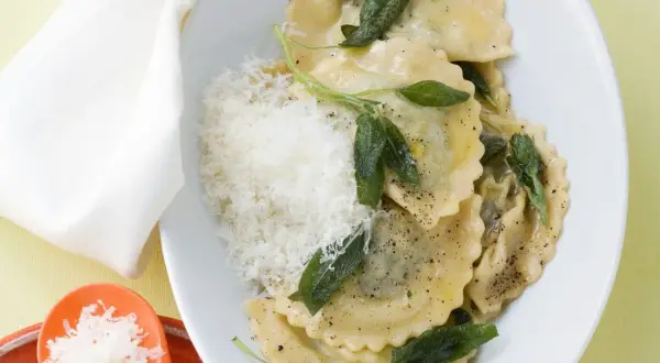 Ravioli mit Spinat-Ricotta-Füllung, Salbeiblättern und geriebenem Parmesan auf einem Teller.