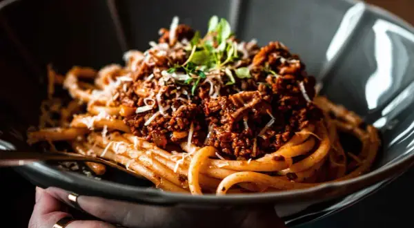 Ein Teller Spaghetti Ragu, garniert mit Parmesan und frischen Kräutern, wartet darauf, genossen zu werden.