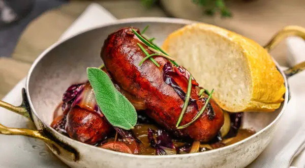 Herzhafte, selbstgemachte Salsiccia mit Rotkohl und Brot in einer Pfanne, garniert mit Salbei und Rosmarin.