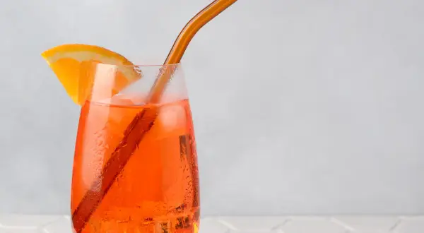 Ein Aperol Spritz mit Orangenscheibe und braunem Strohhalm auf Eis.