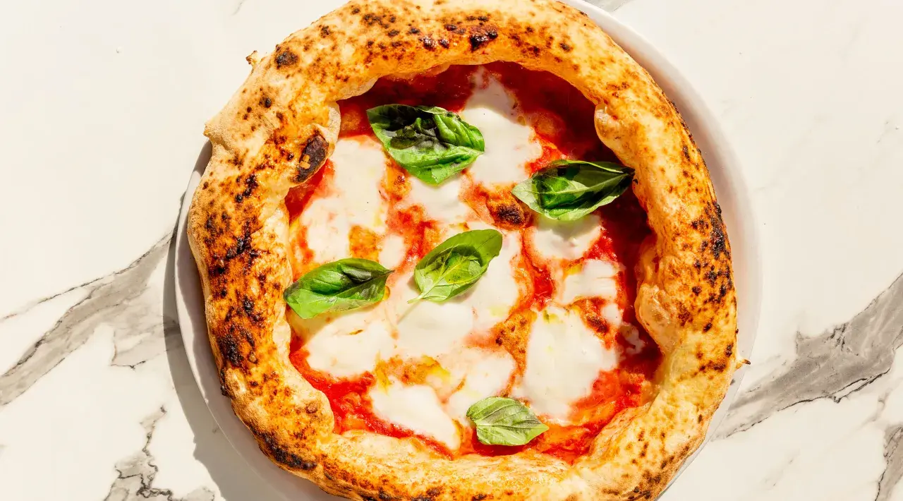 Eine köstliche Pizza Margherita mit geschmolzenem Mozzarella, Tomatensauce und frischem Basilikum auf einem Marmortisch.