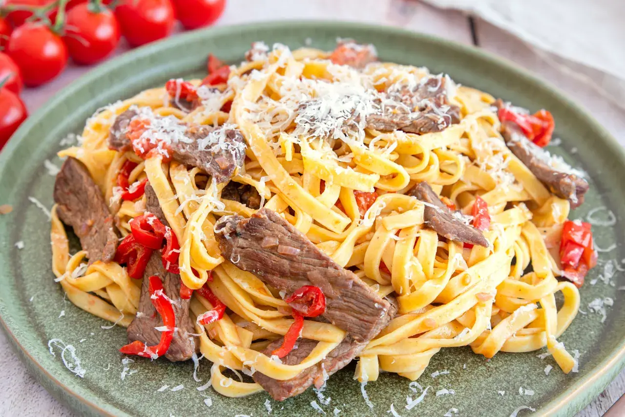 Pasta mit Rinderfiletstreifen, garniert mit geriebenem Parmesan und roten Paprikastücken. Ein köstliches Gericht, das zum Genießen einlädt.