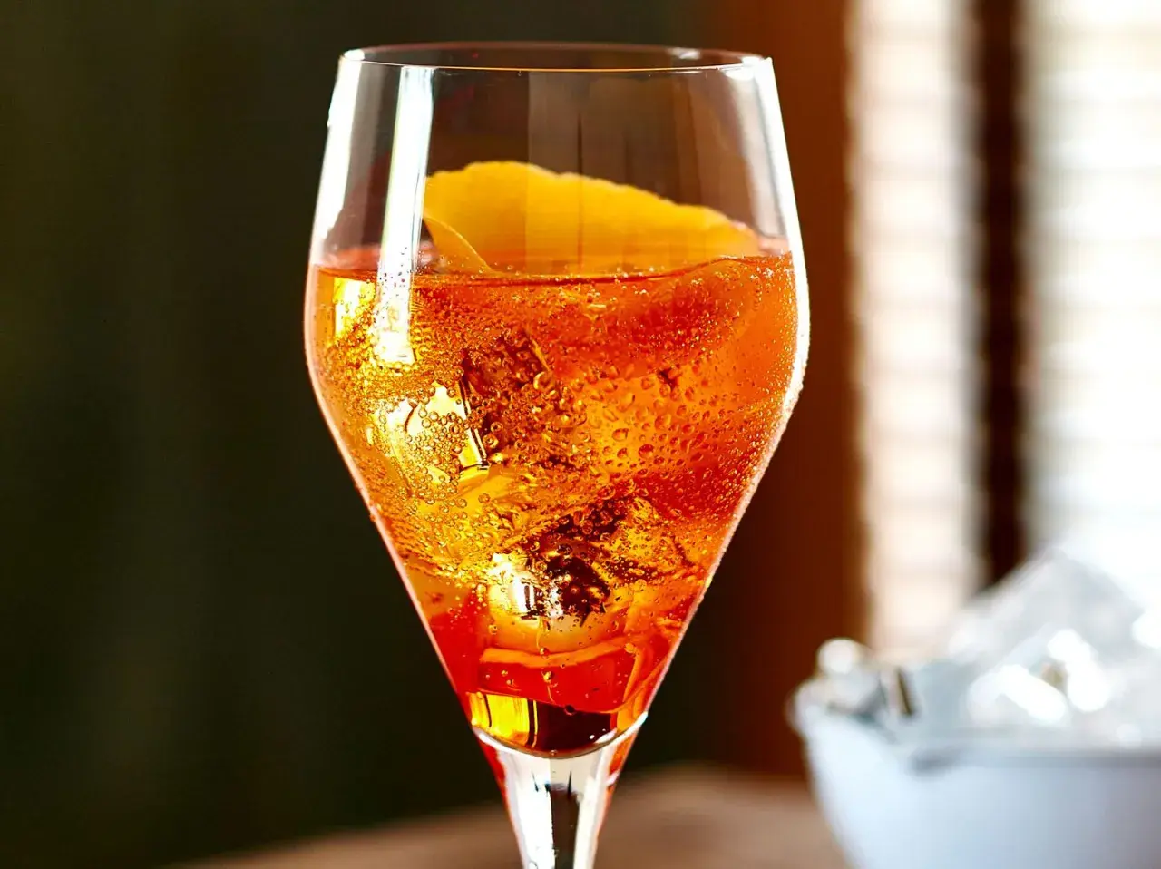 Ein Aperol Sour im Glas mit Eiswürfeln und Orangenzeste, Bläschen steigen auf.