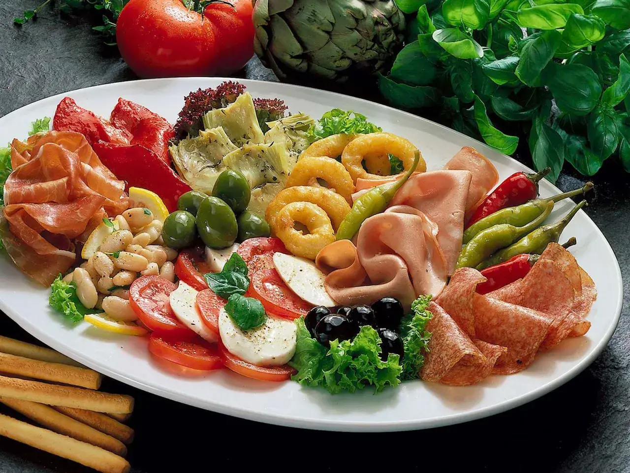 Eine reichhaltige Antipasti-Platte mit Wurst, Käse, Gemüse, Oliven und Brotstangen.