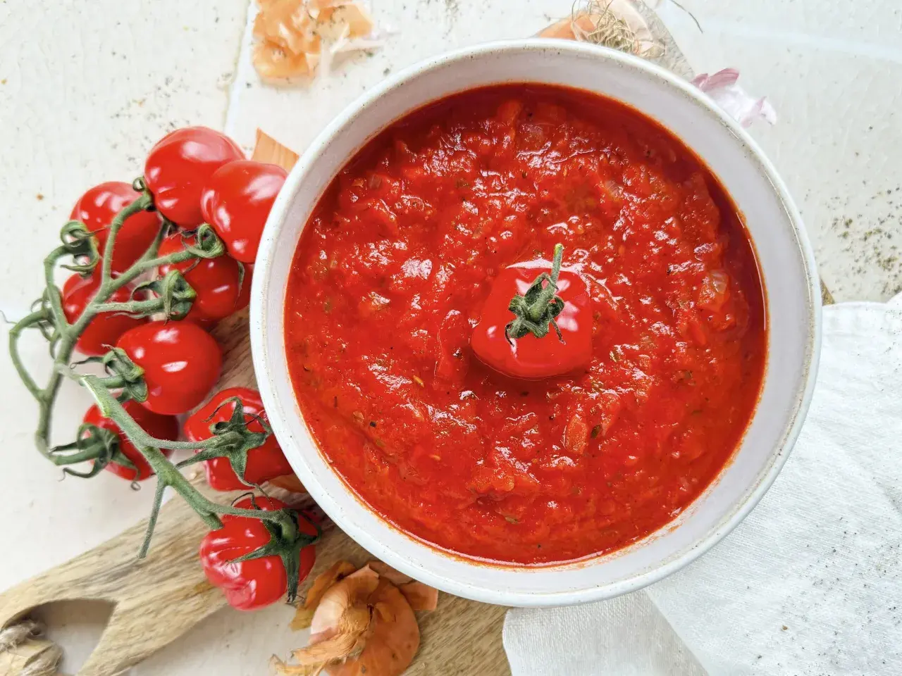 Eine Schüssel mit hausgemachter marinara sauce, garniert mit einer Kirschtomate, daneben frische Tomaten und Zwiebeln.