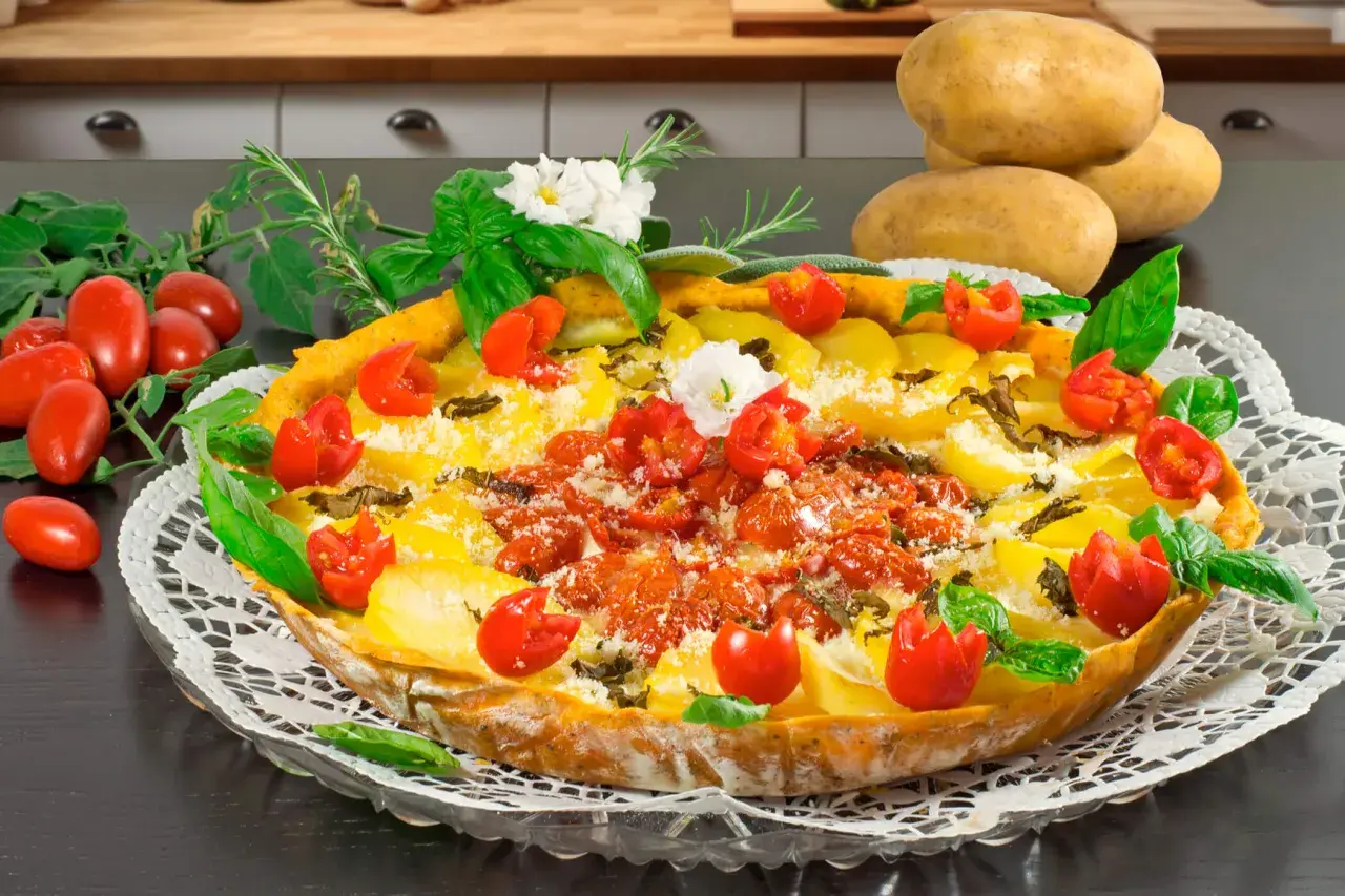 Herzhafte torta salata mit Kartoffeln, Tomaten und Kräutern, garniert mit frischem Basilikum und kleinen weißen Blüten.