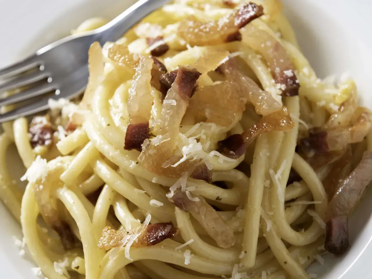 Ein Teller Pasta mit knusprigen Speckwürfeln, die zeigen, was ist Guanciale: luftgetrockneter Schweinebackenspeck, der für den authentischen Geschmack sorgt.
