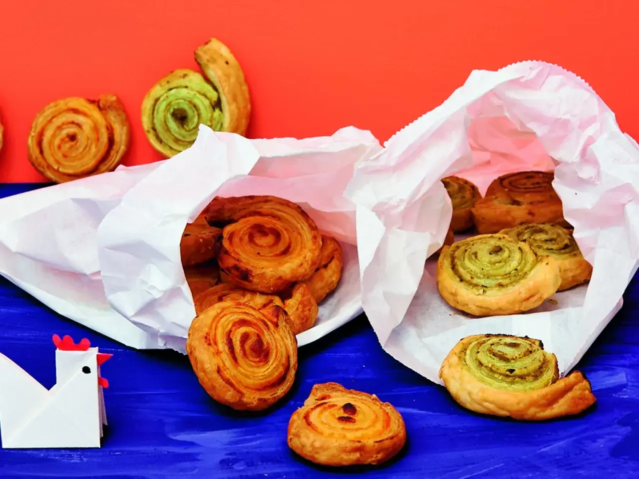Zwei weiße Papiertüten quellen über mit köstlichen Pesto-Schnecken. Einige sind goldbraun, andere mit grünem Pesto gefüllt.