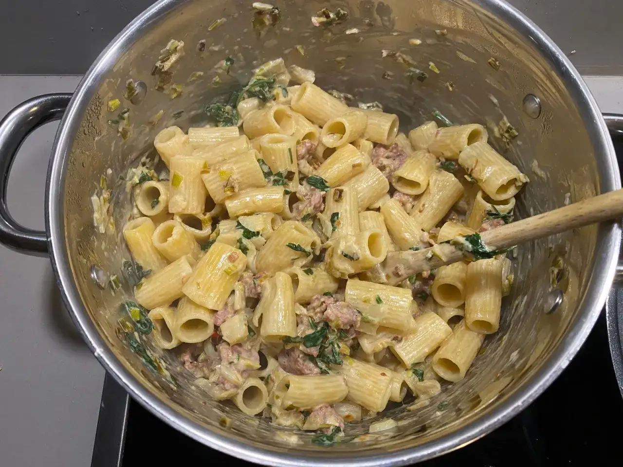 Rigatoni mit cremiger Sauce, Fenchel und Salsiccia. Ein Holzlöffel rührt die köstliche Pasta in einem Topf.