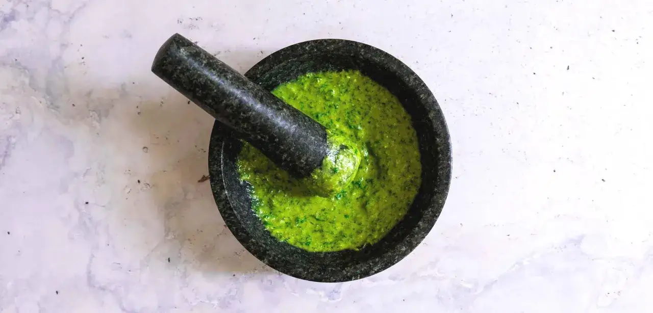 Frisch zubereitetes, leuchtend grünes Pesto Genovese in einem Mörser aus Granit. Der Stößel liegt darin.