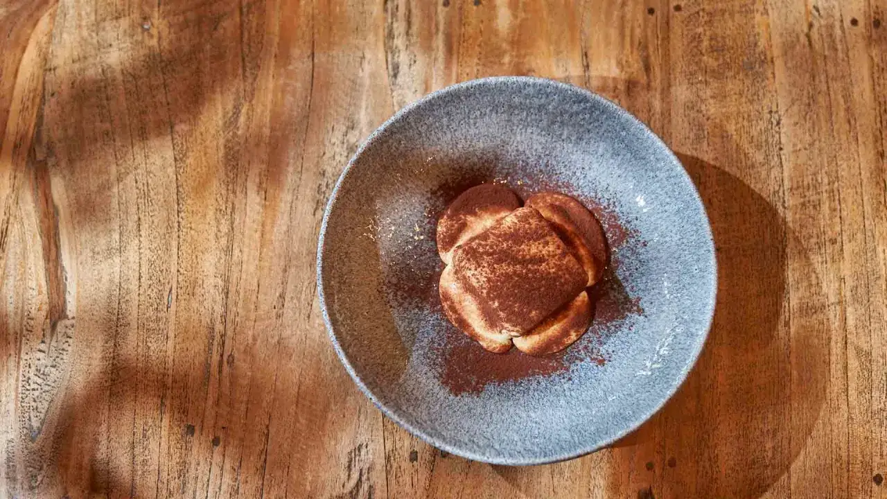 Ein köstliches Tiramisu, das nach einem original italienischen Rezept zubereitet wurde, bestäubt mit Kakao, serviert auf einem rustikalen Holztisch.