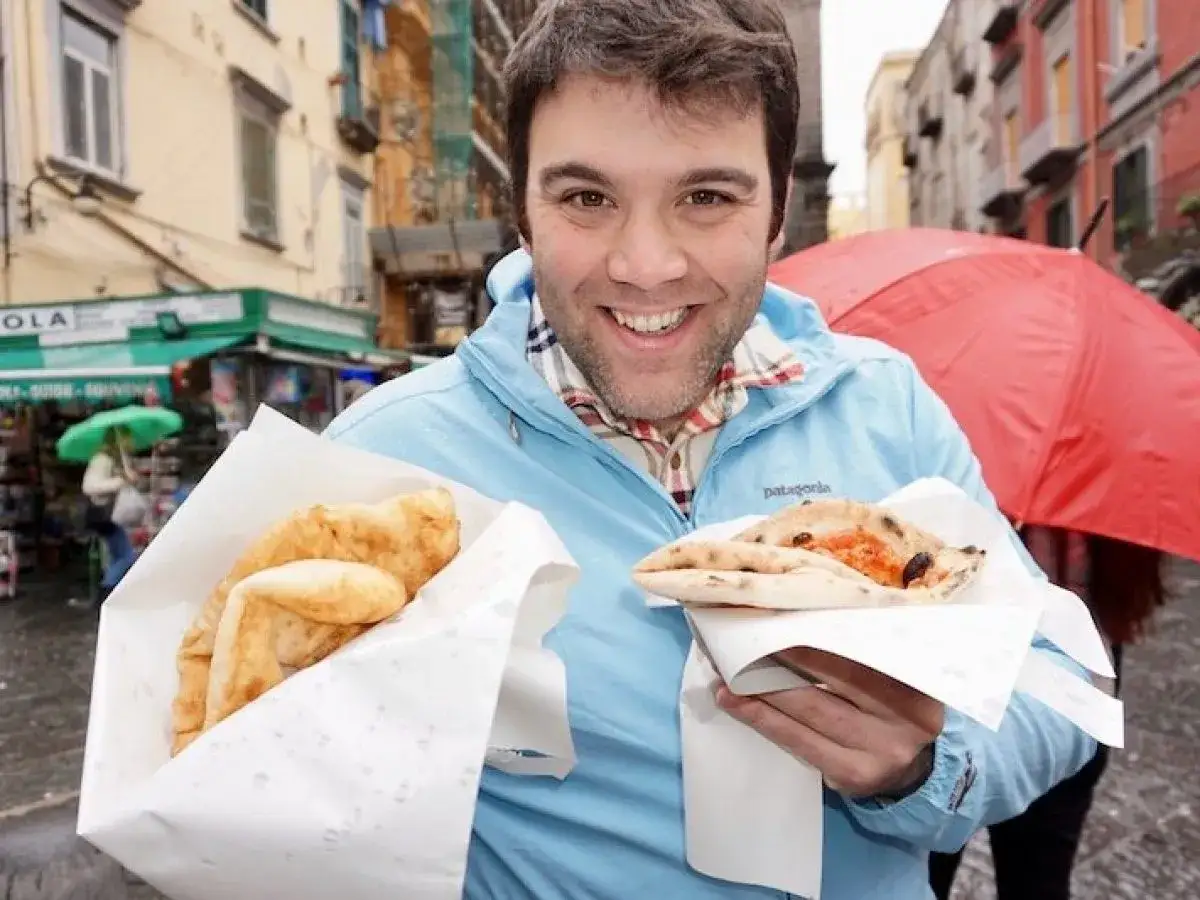 Mann hält frittierte Pizza und Pizza a portafoglio, typisches Neapel Essen, vor bunten Häusern.