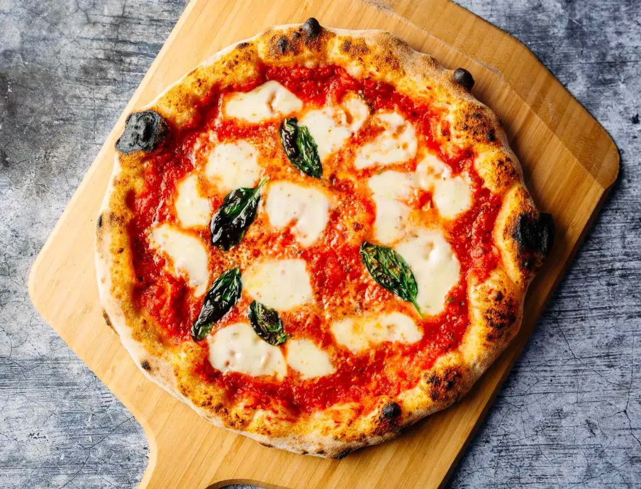Eine klassische Pizza Margherita mit geschmolzenem Mozzarella, Tomatensauce und frischem Basilikum auf einem Holzbrett.