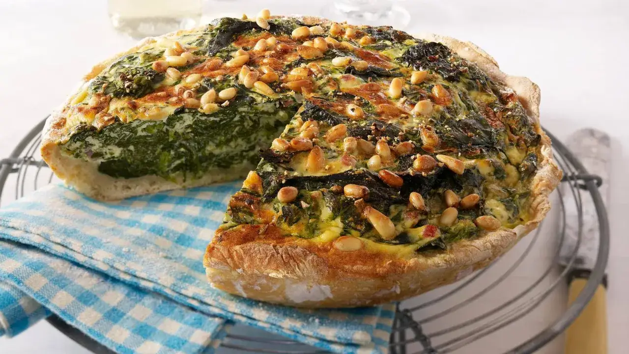 Herzhafte torta salata mit Spinat, Pinienkernen und Käse, auf einem karierten Tuch serviert.