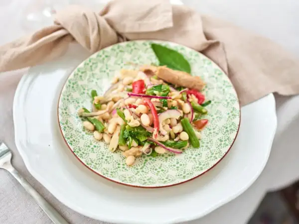 Ein bunter Thunfisch-Bohnen-Salat, italienisch inspiriert, mit grünen Bohnen, roten Zwiebeln und Tomaten auf einem Teller mit grünem Muster.