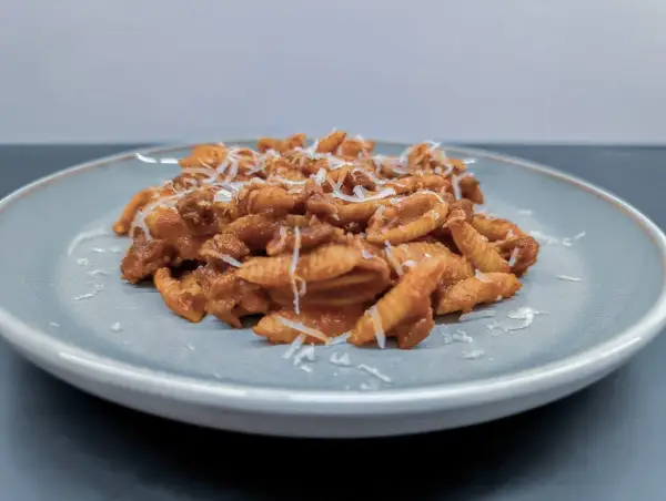 Gnocchi Sardi (Malloreddus) mit Tomatensoße und geriebenem Parmesan auf einem Teller.