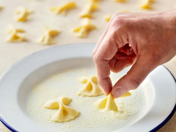 Hand formt frische Farfalle für leckere Farfalle Rezepte. Viele kleine Nudelschmetterlinge liegen bereit.