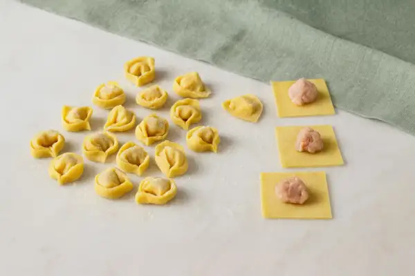 Frische Tortellini und Teigquadrate mit Füllung auf Marmorplatte.