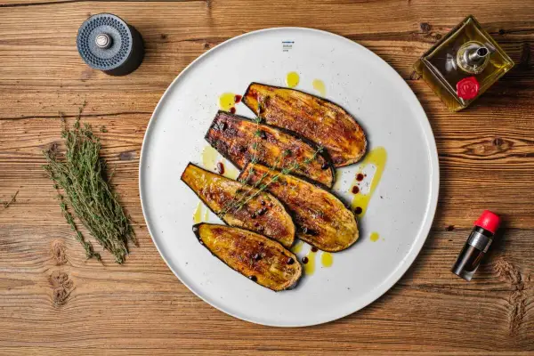 Gegrillte Auberginenscheiben als Antipasti, beträufelt mit Olivenöl und Balsamico, garniert mit Thymian.