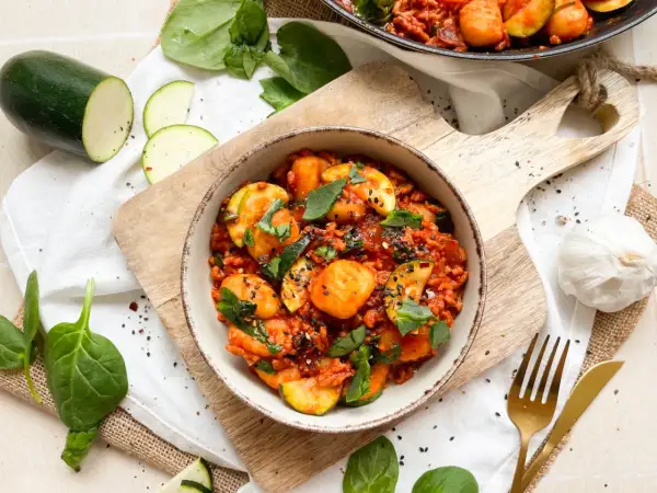 Gnocchi mit Spinat und Zucchini in Tomatensauce, garniert mit schwarzen Sesam.