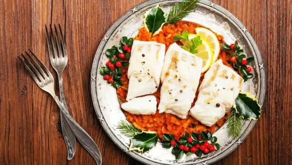 Gedünsteter Fisch auf Tomatenragout, festlich dekoriert mit Beeren und Tannenzweigen. Ein Gericht, das an italienische Weihnachtsrezepte erinnert.